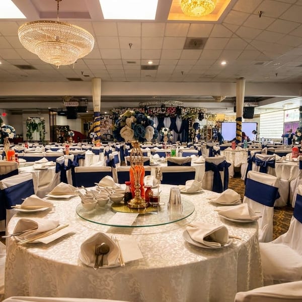 A large banquet hall with round tables set with white tablecloths and chairs with navy blue sashes.