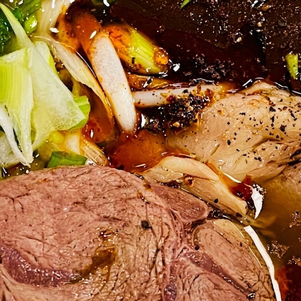 Close-up of a Vietnamese noodle soup with beef, green onions, and chili oil.