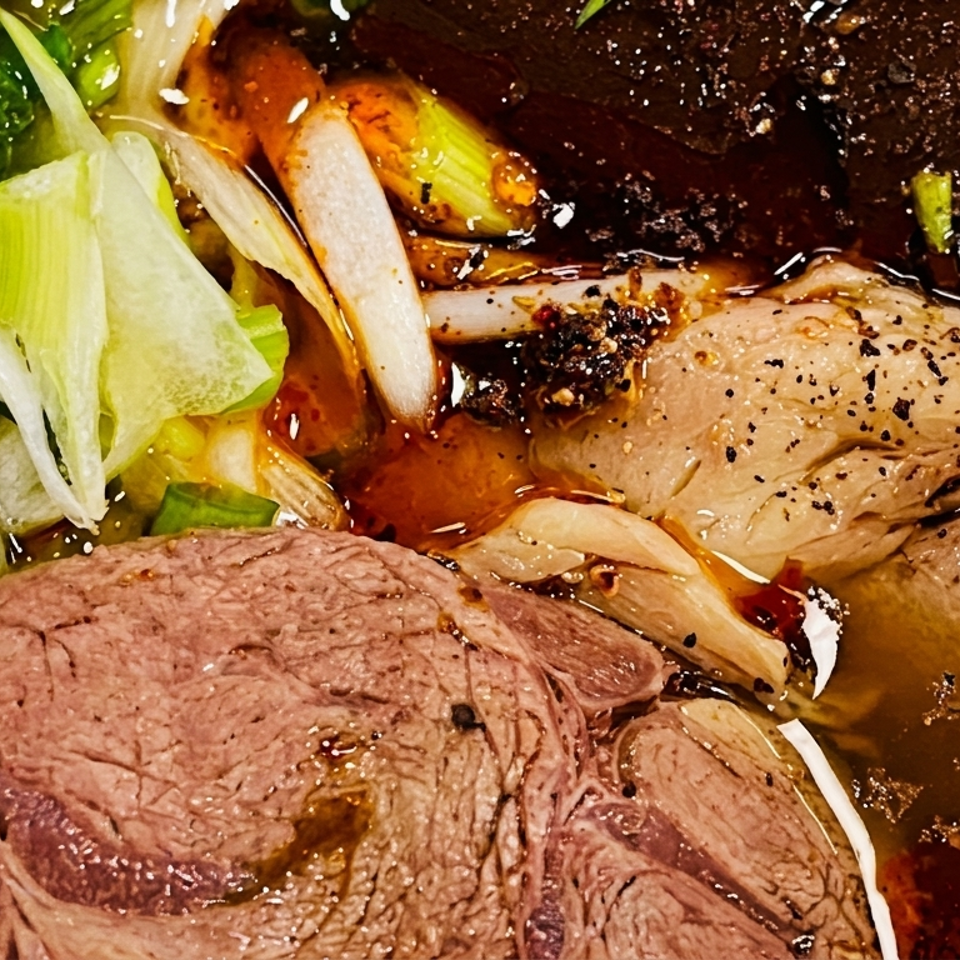 Close-up of a Vietnamese noodle soup with beef, green onions, and chili oil.