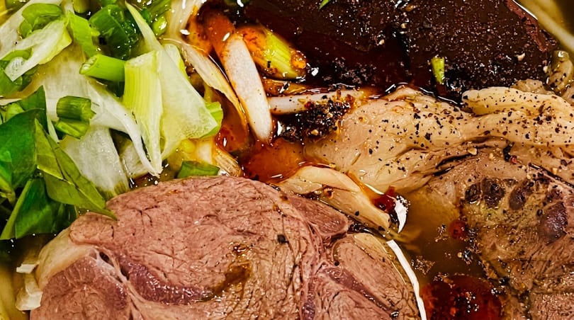 Close-up of a Vietnamese noodle soup with beef, green onions, and chili oil.