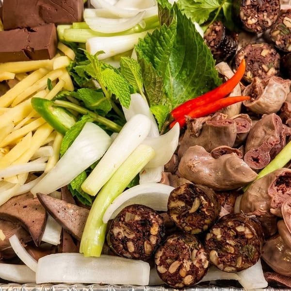 A tray of Vietnamese Thit Heo Luoc, with sliced pork, blood sausage, herbs, and vegetables.