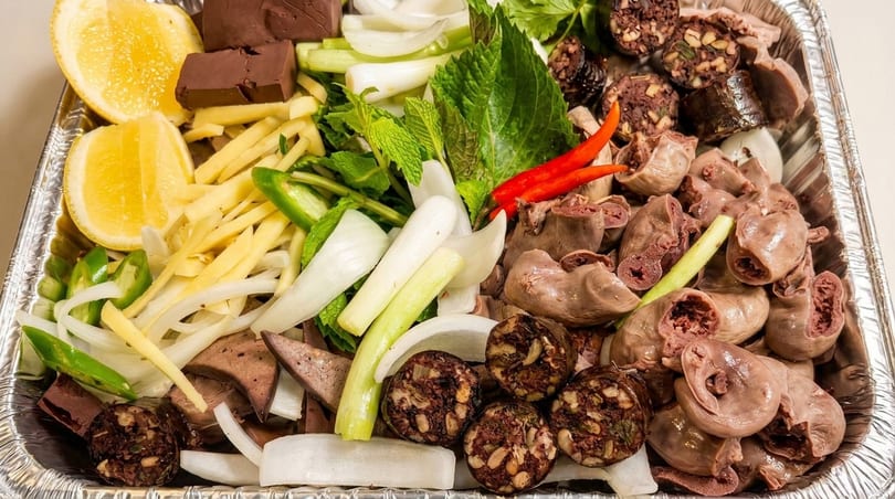 A tray of Vietnamese Thit Heo Luoc, with sliced pork, blood sausage, herbs, and vegetables.
