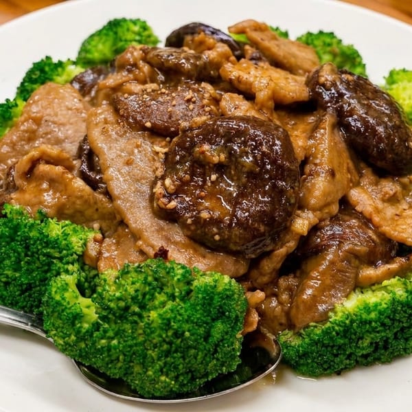 Braised pork with shiitake mushrooms and broccoli florets on a white plate with a spoon.